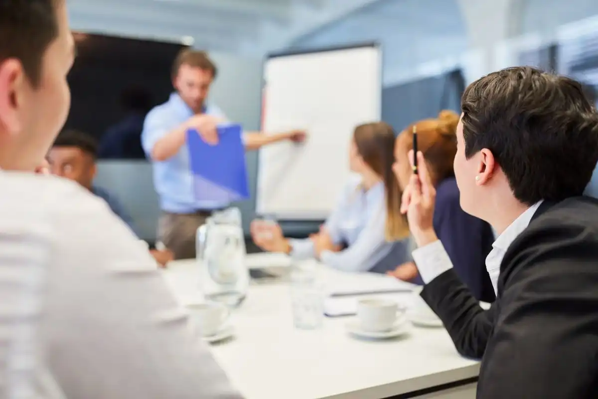 Groupe de professionnels en réunion de formation, écoutant une présentation avec un formateur utilisant un tableau blanc, reflétant un environnement d'apprentissage en entreprise et le développement des compétences.