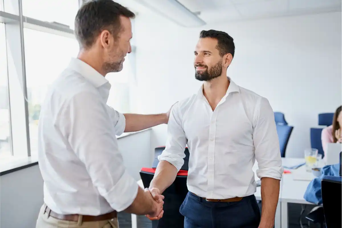 Deux hommes d'affaires se serrant la main dans un bureau, symbolisant l'accueil d'un nouvel employé ou une conclusion positive de recrutement, dans un environnement professionnel.