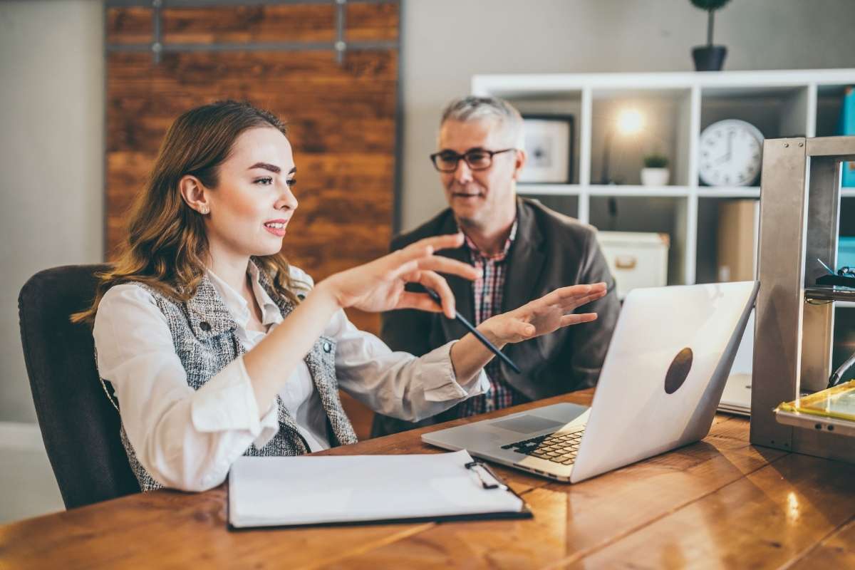 Une femme et un homme discutent devant un ordinateur portable dans un bureau moderne, illustrant le but du mentorat en carrière.